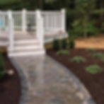 Stone paver walkway leading to a white deck with stairs.