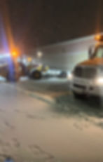 Commercial snow removal trucks clearing a lot at night.