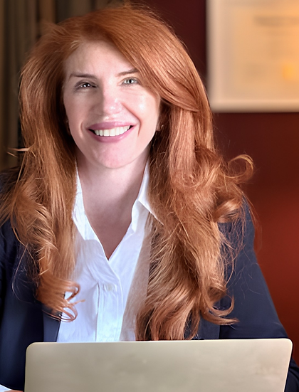 Smiling red-haired woman at desk with laptop in home office.