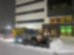 Commercial snow plow clearing office parking lot at night.