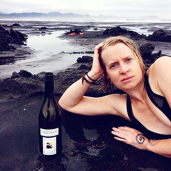A woman poses with a wine bottle on a beach at Kawhia New Zealand