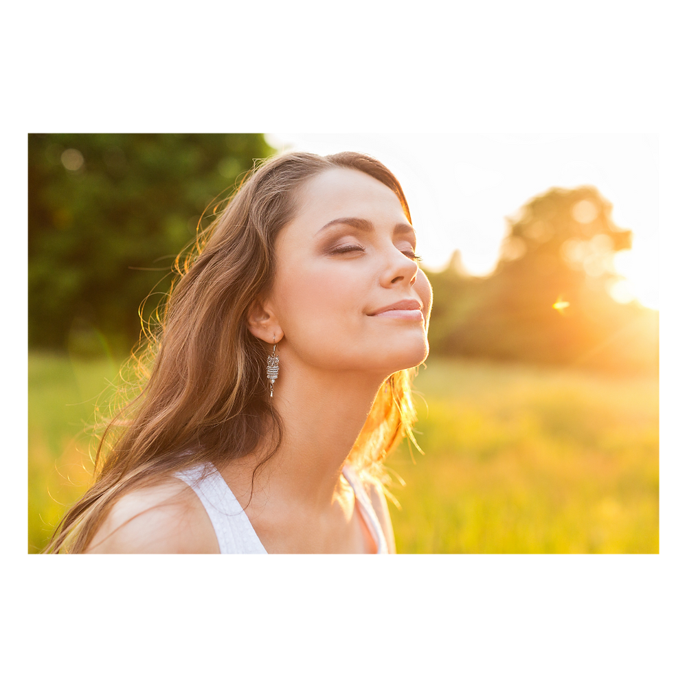 Imagem em que uma mulher sorri de olhos fechados sentindo o calor do amanhecer.