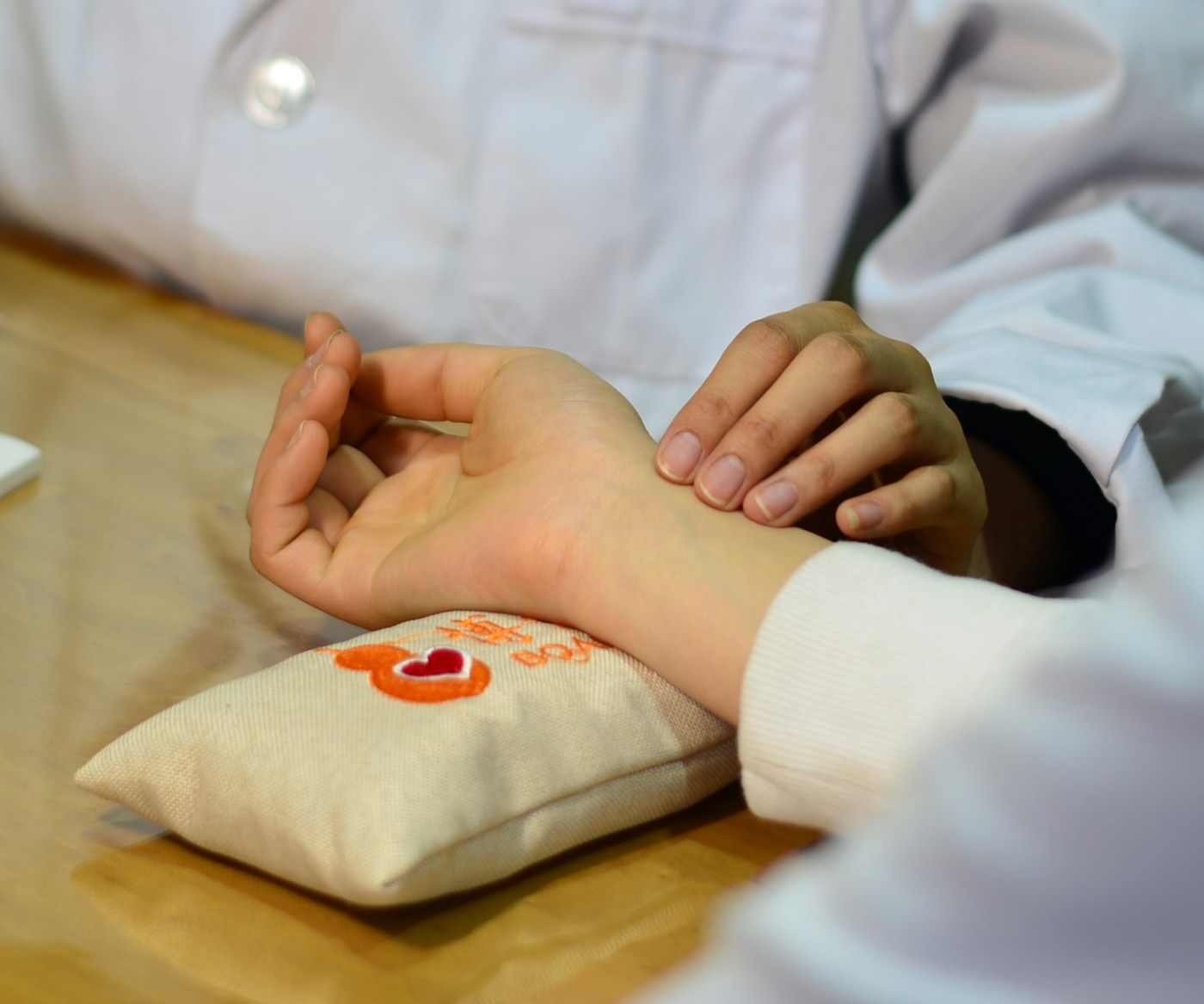 Pulsdiagnose: Finger tasten den Puls am Handgelenk, das auf einem Pulskissen liegt