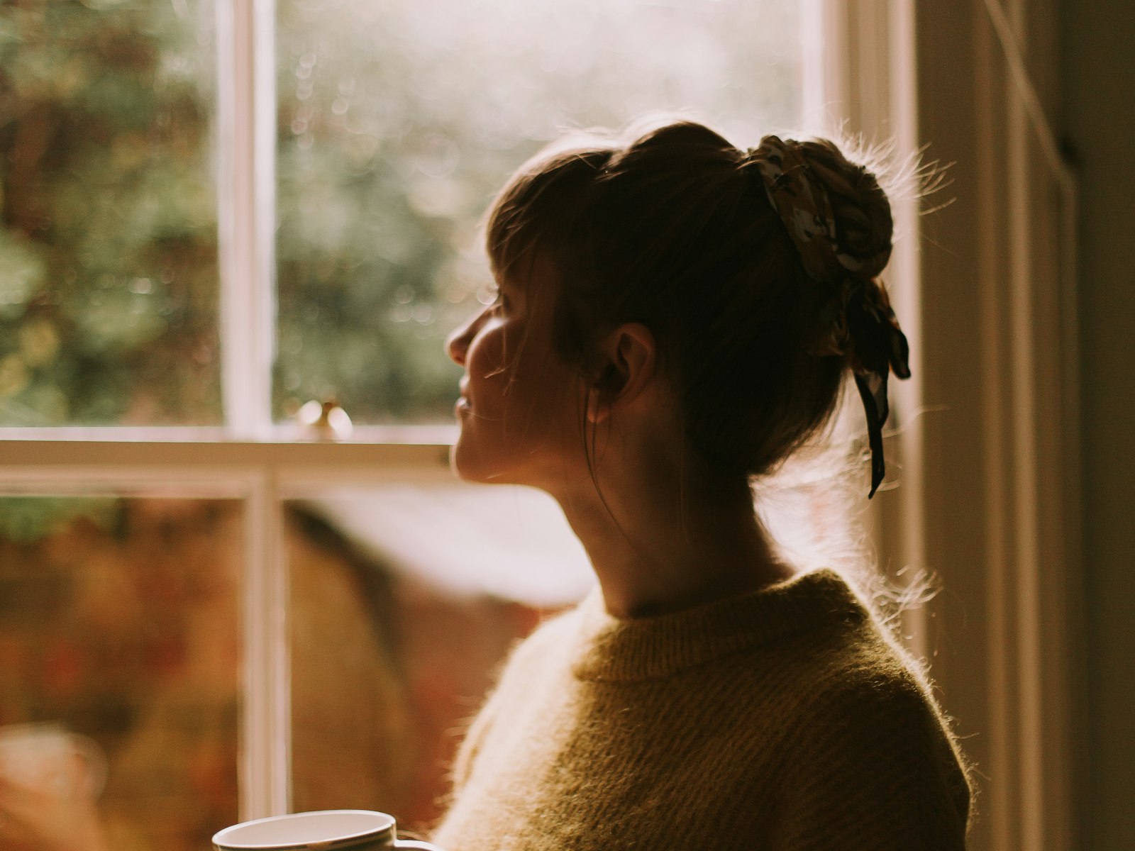 Frau mit Tasse am Fenster im warmen Gegenlicht
