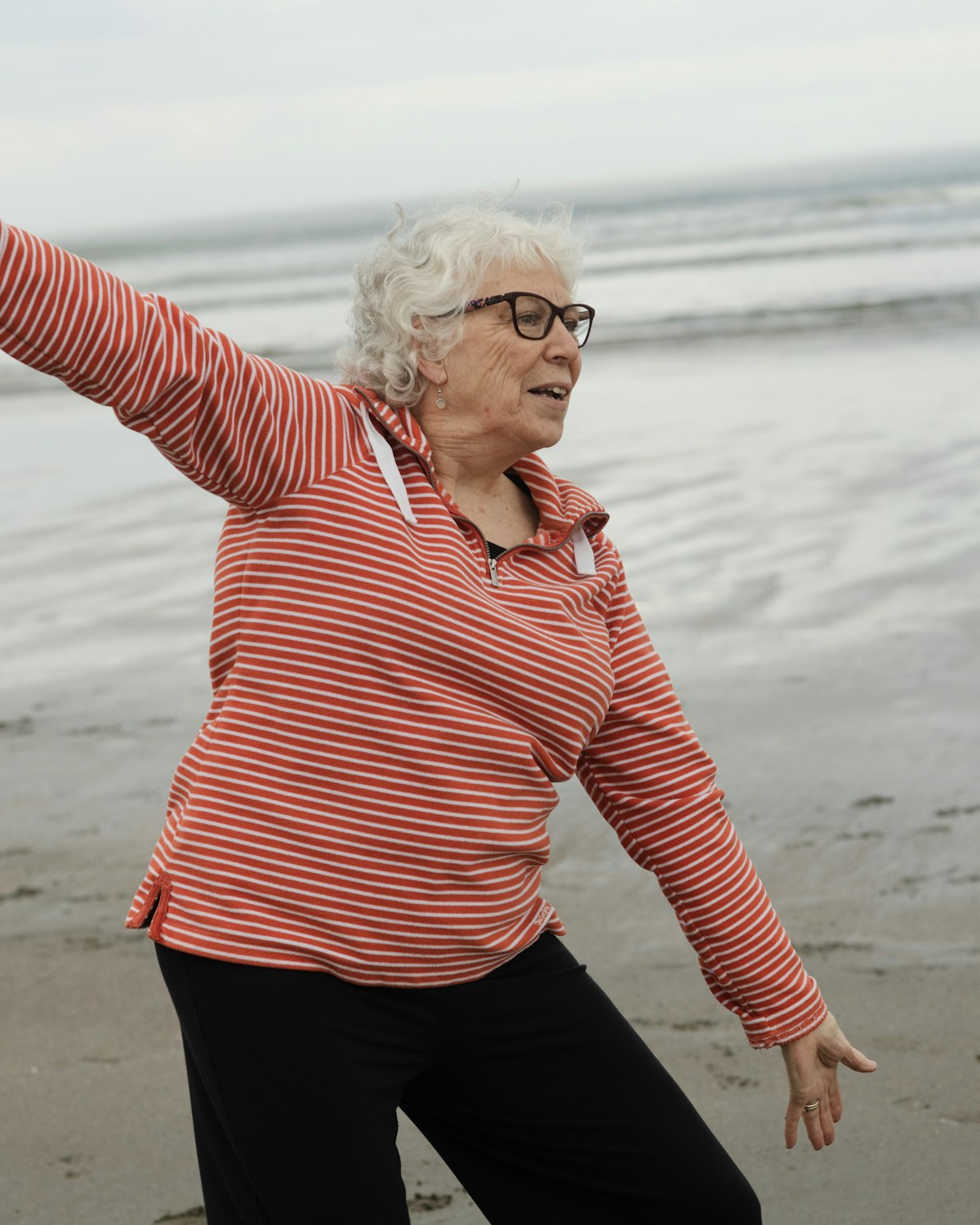 Ältere Frau übt Tai Chi am Strand, die Arme weit ausgebreitet
