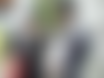 共働きの両親がスーツ姿で笑顔を交わしながら、父親が抱っこひもで赤ちゃんを抱えている様子。自宅前の朝の出勤風景で、忙しい中でも家族の絆を感じさせるシーン。