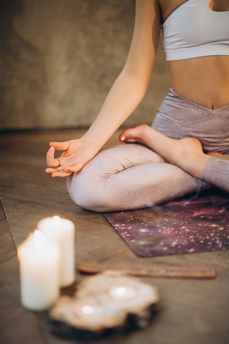 A girl sits in meditation pose with candles lit on the ground.
