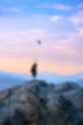 A girl on a mountain throws a graduation cap in the air.
