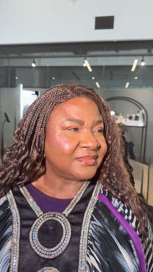 Soft glam makeup on a dark-skinned client with mature skin, featuring smooth radiant coverage, defined eyes, and a natural glossy lip, captured in a salon setting.