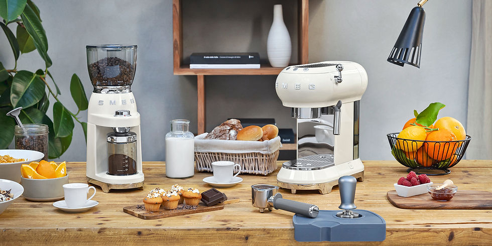 Miniaturbild: Cremefarbene Espressomaschine von SMEG auf Holztisch mit Milch, Kaffeebohnen, Gebäck, Schokolade und Zubehör vor Regal