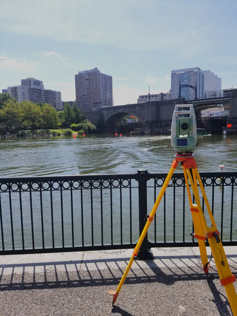 Surveying tripod and instrument by a river with city buildings and bridge in the background