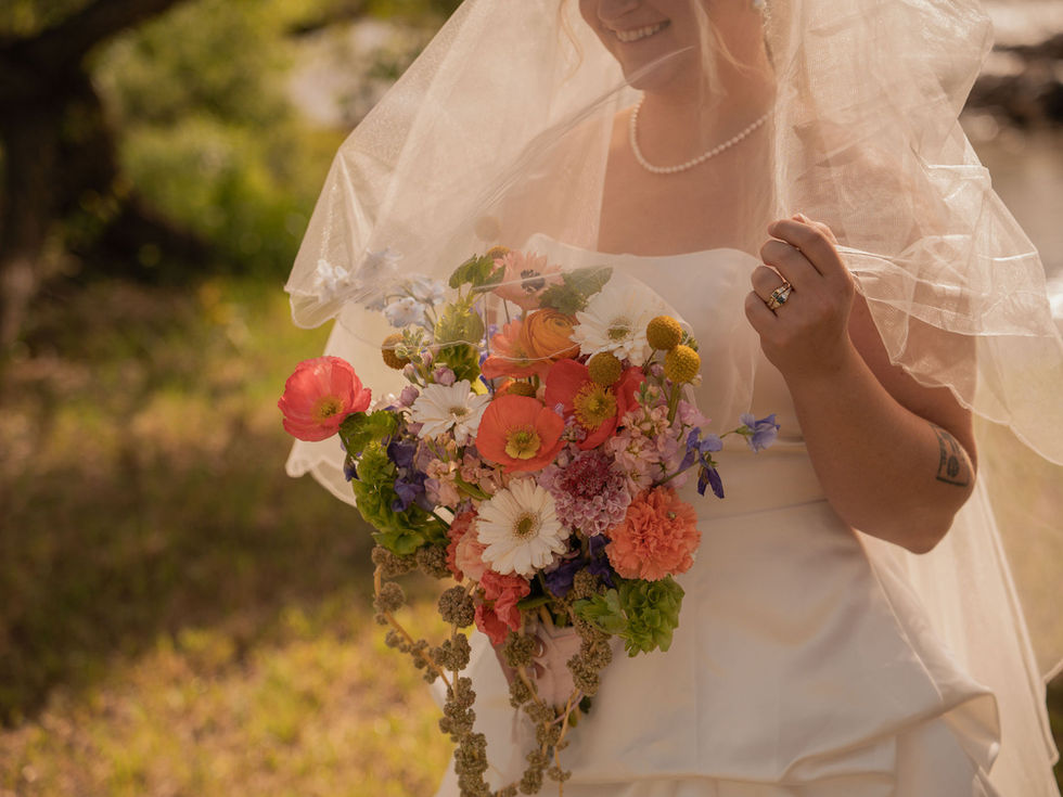 Bride holding a bright eclectic bouquet featuring orange, coral, pink, yellow, white and lime green flowers with playful modern styling