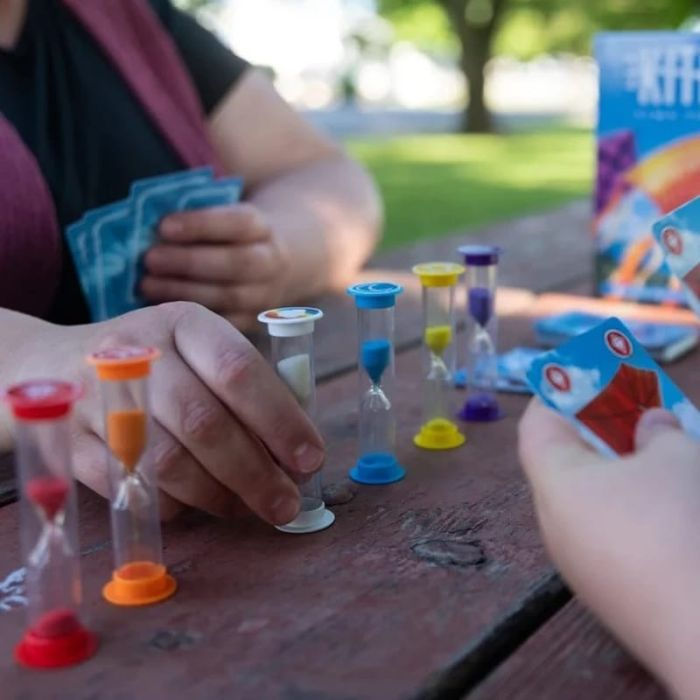 Mani giocano a un gioco da tavolo con clessidre colorate su tavolo picnic.