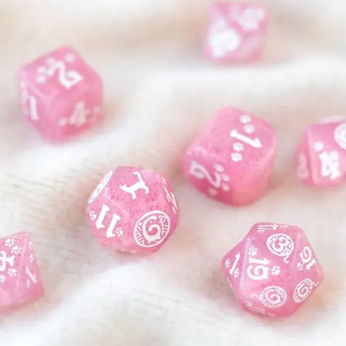 Dadi rosa traslucidi con numeri e motivi bianchi sparsi su superficie morbida.