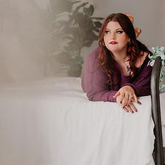 woman lying on iron bed covered with beige blanket with hands posed on top of one another