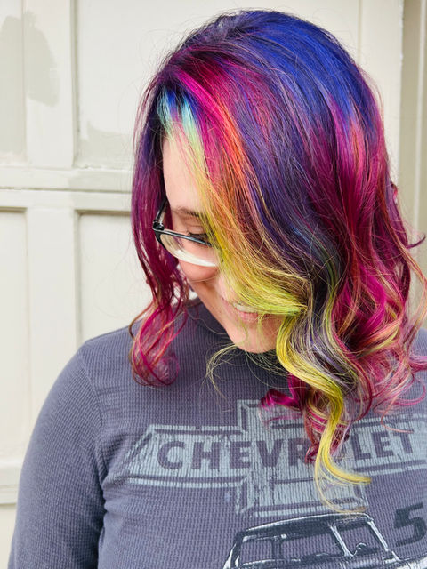 Woman with colorful hair and glasses, Chevy shirt smiles. EJS Beauty Denver Services