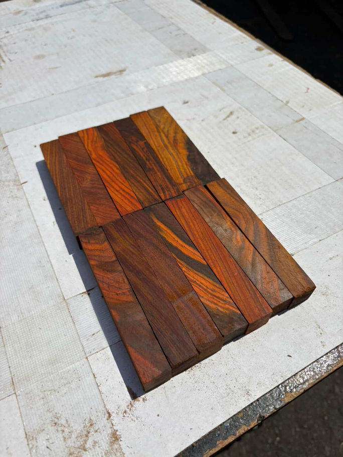 Several Cocobolo King Pen Blanks arranged on a white surface with beautiful wood grains.