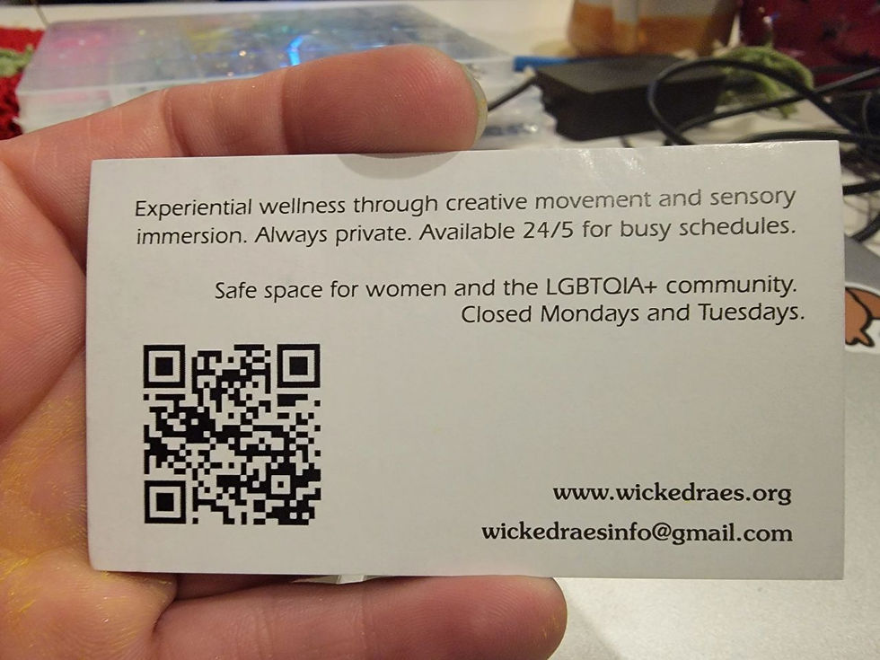 Hand holds business card with QR code and text about Wicked Rae's experiential wellness, private 24/5 safe space for women and LGBTQIA+ community.