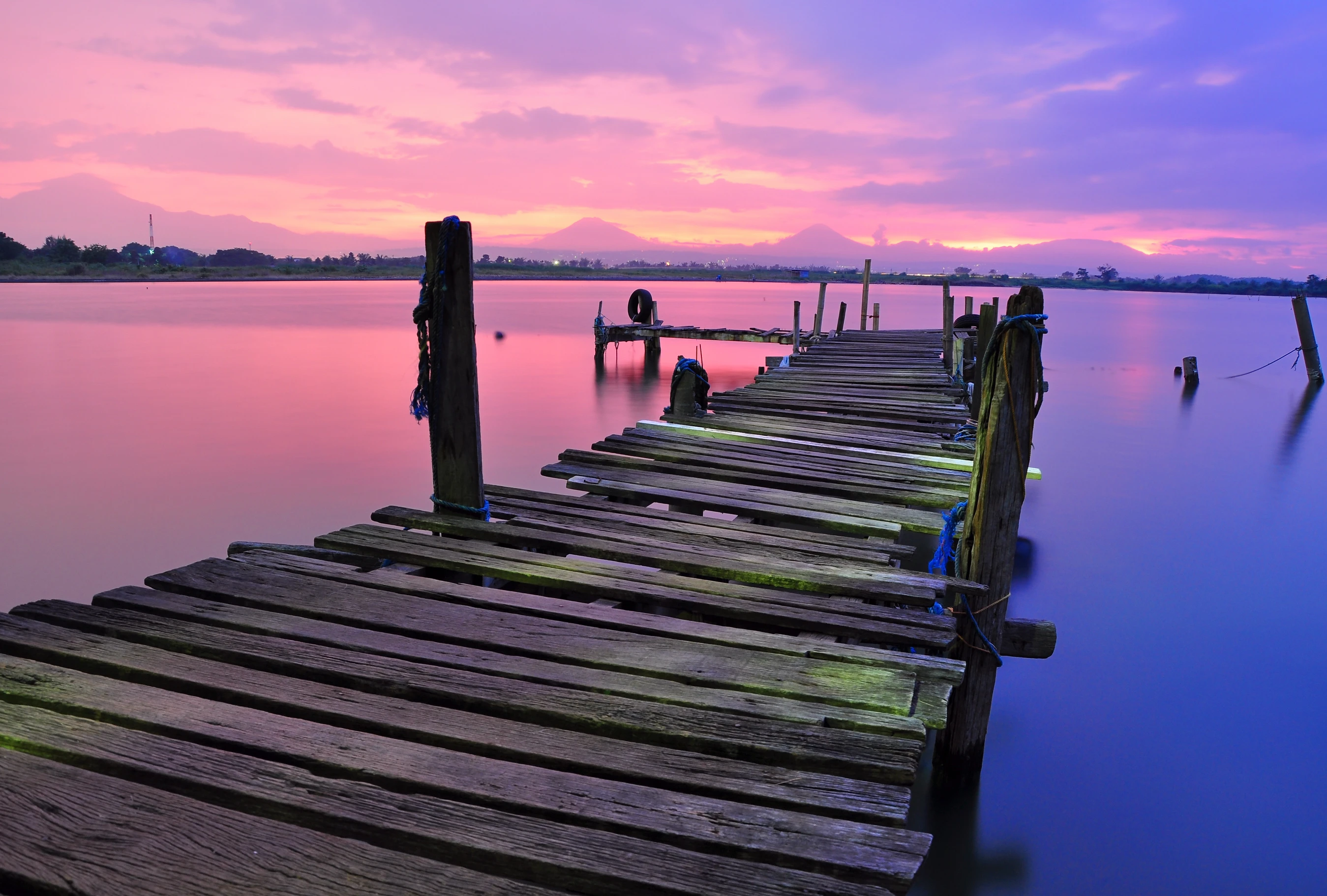 wooden dock leading over the water of a lake during a sunset where the sky is pink and purple and reflected in the water