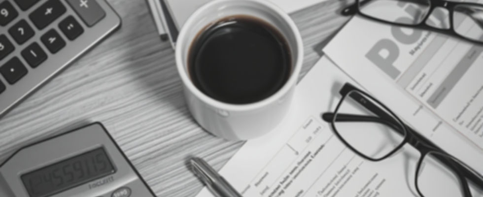 a black & white image of an office desk with a cup of coffee, calculator, pen, reading gla
