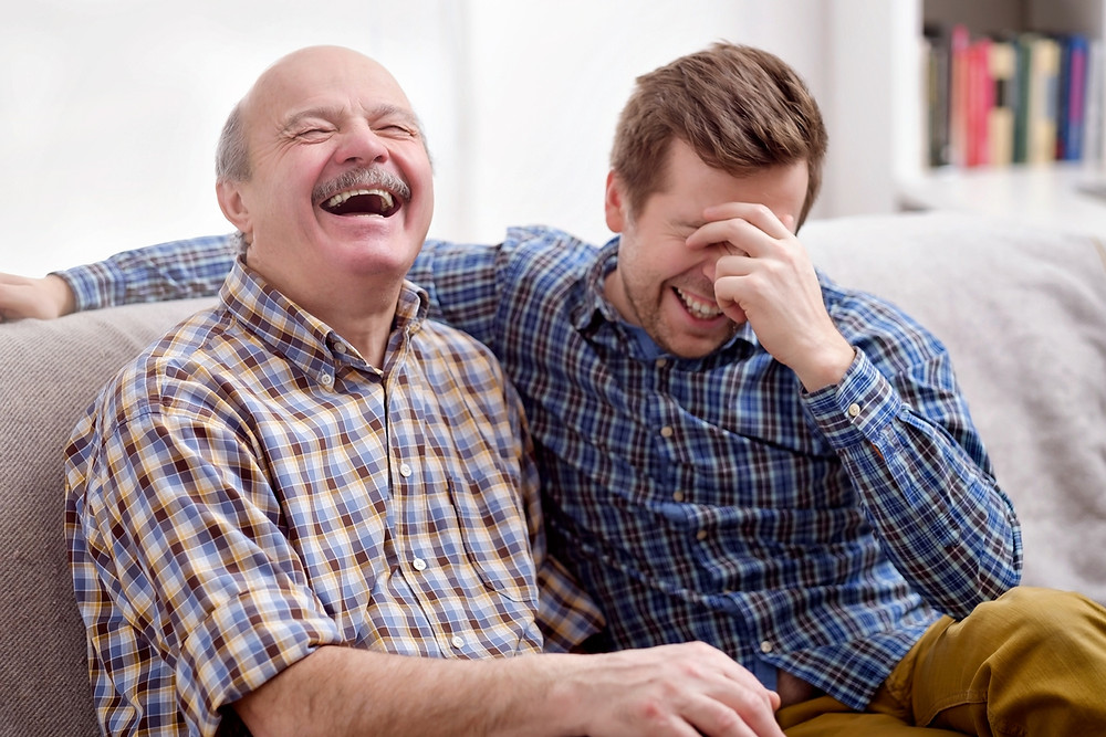 Father and son sitting on a couch, both are laughing, dad told a joke