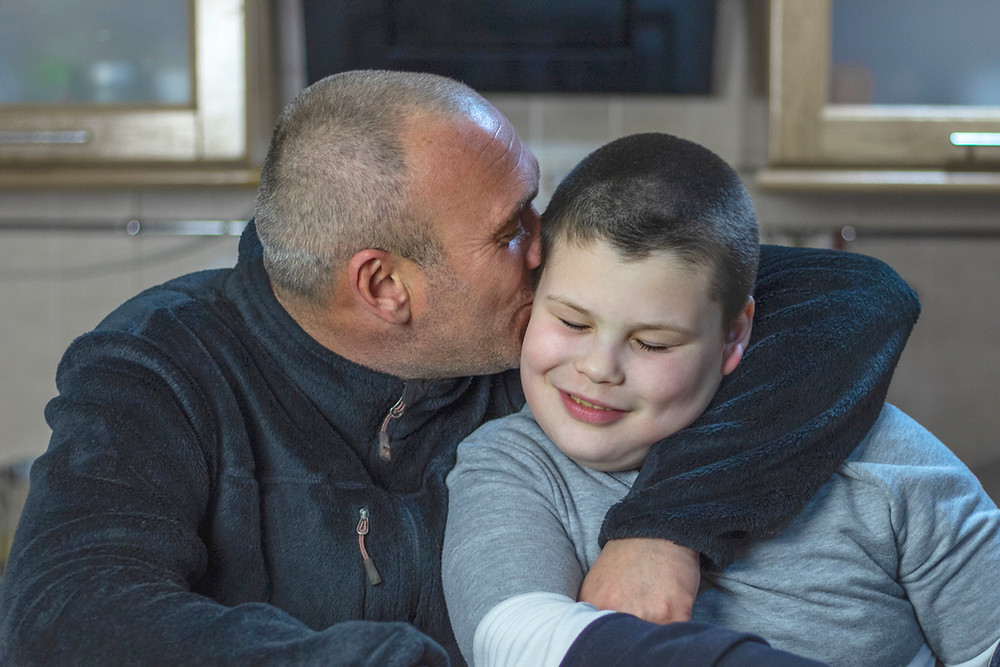 Grandpa sitting beside grandson, kissing grandson on the cheek