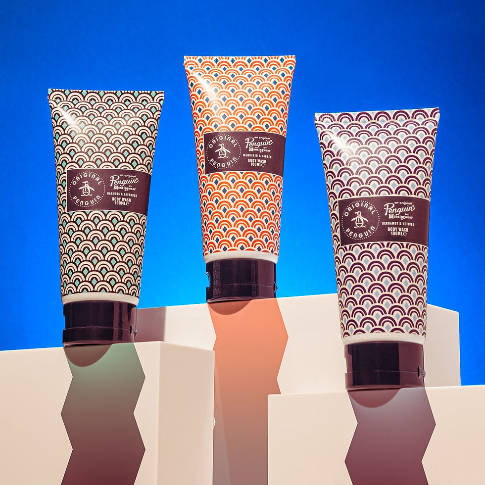 Three patterned body wash tubes on geometric podiums against a vivid blue background. Labels feature a penguin logo and product details.