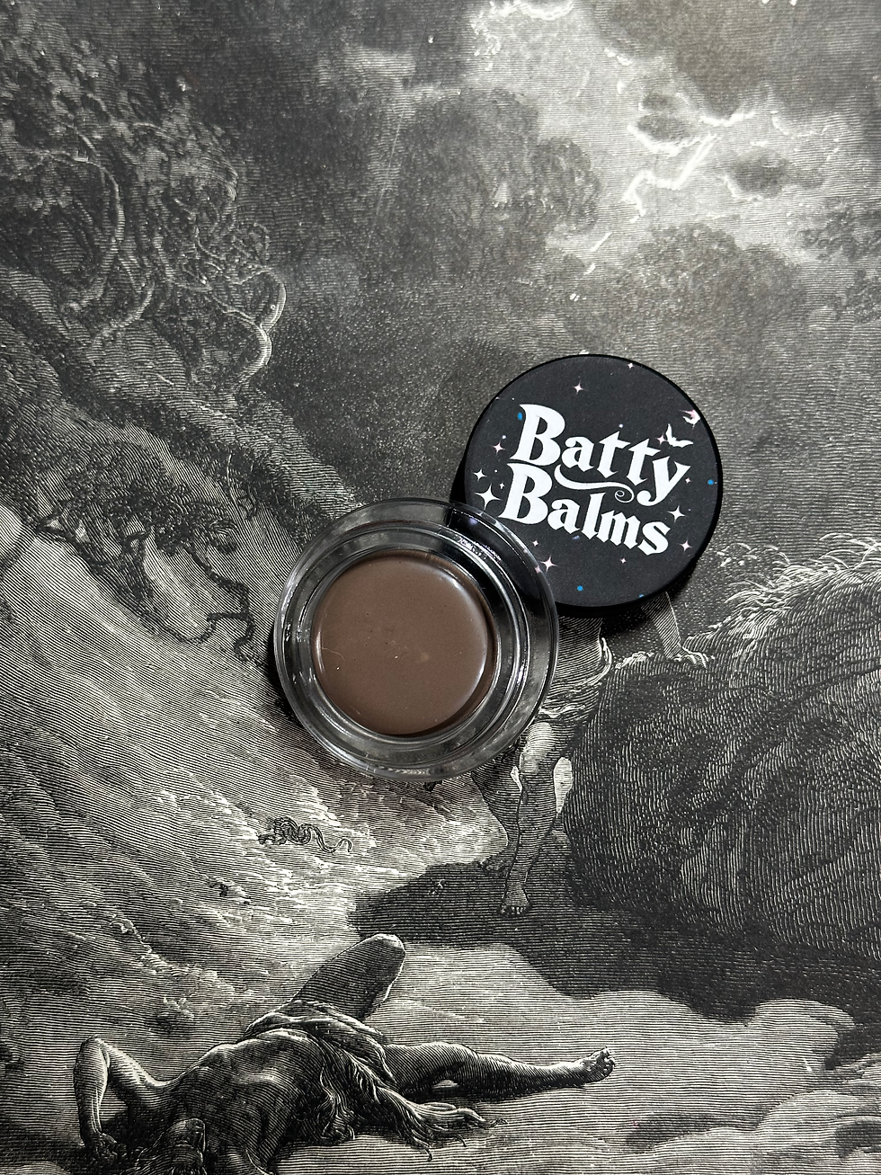 Batty Balms eyeshadow pot with lid open on gothic background.