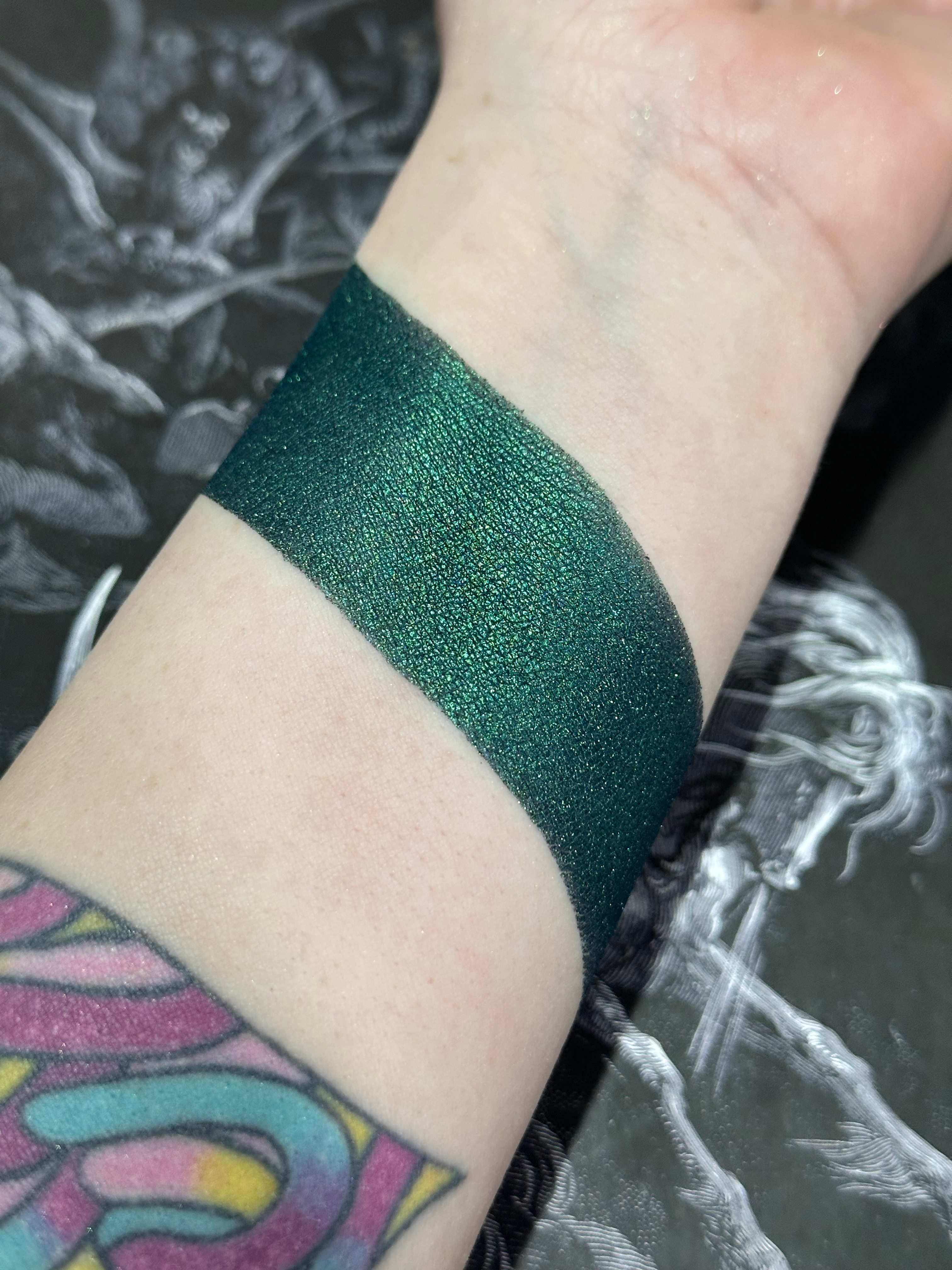 Swatched Gethsemane - Metallic Dark Green Pressed Eyeshadow on wrist, showcasing pigment and shimmer.