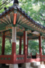 Colorful traditional pavilion with intricate patterns and calligraphy, set in a lush green forest, evokes a serene, cultural ambiance.