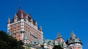 Historic castle-like hotel, Chateau Frontenac, with red brick walls and green copper turrets under a clear blue sky.