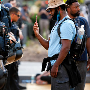 A Black man aims a cellphone at a group of police officers standing less than a foot away from him 