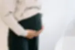 A close up of a Black woman's hands cradling her pregnant belly. She wears black trousers and a beige top.