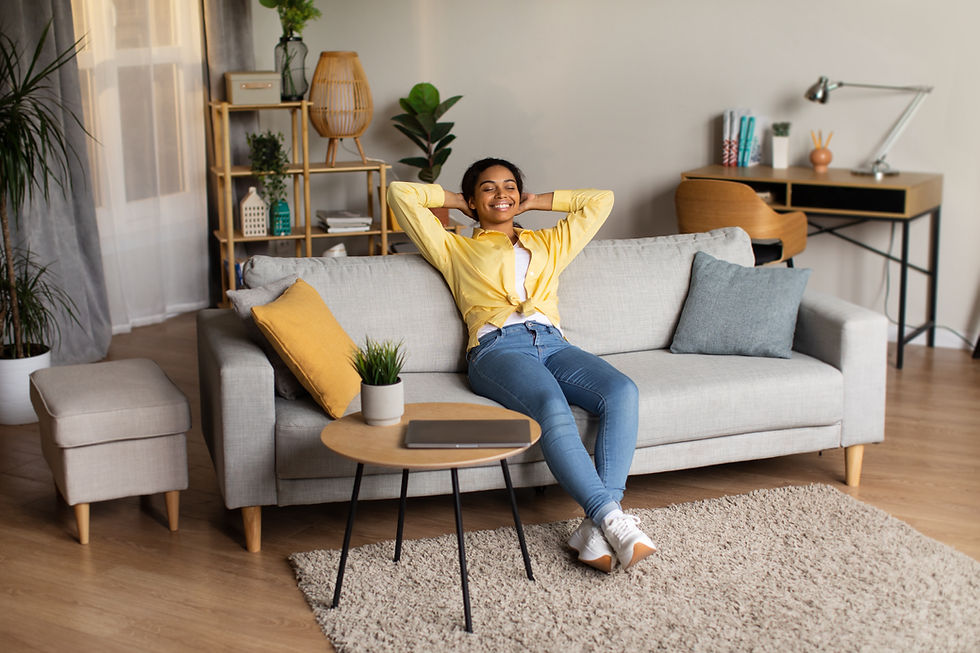 A lightskinned Black woman leans back on a couch and smiles. Her laptop computer sits closed on a table next to her.