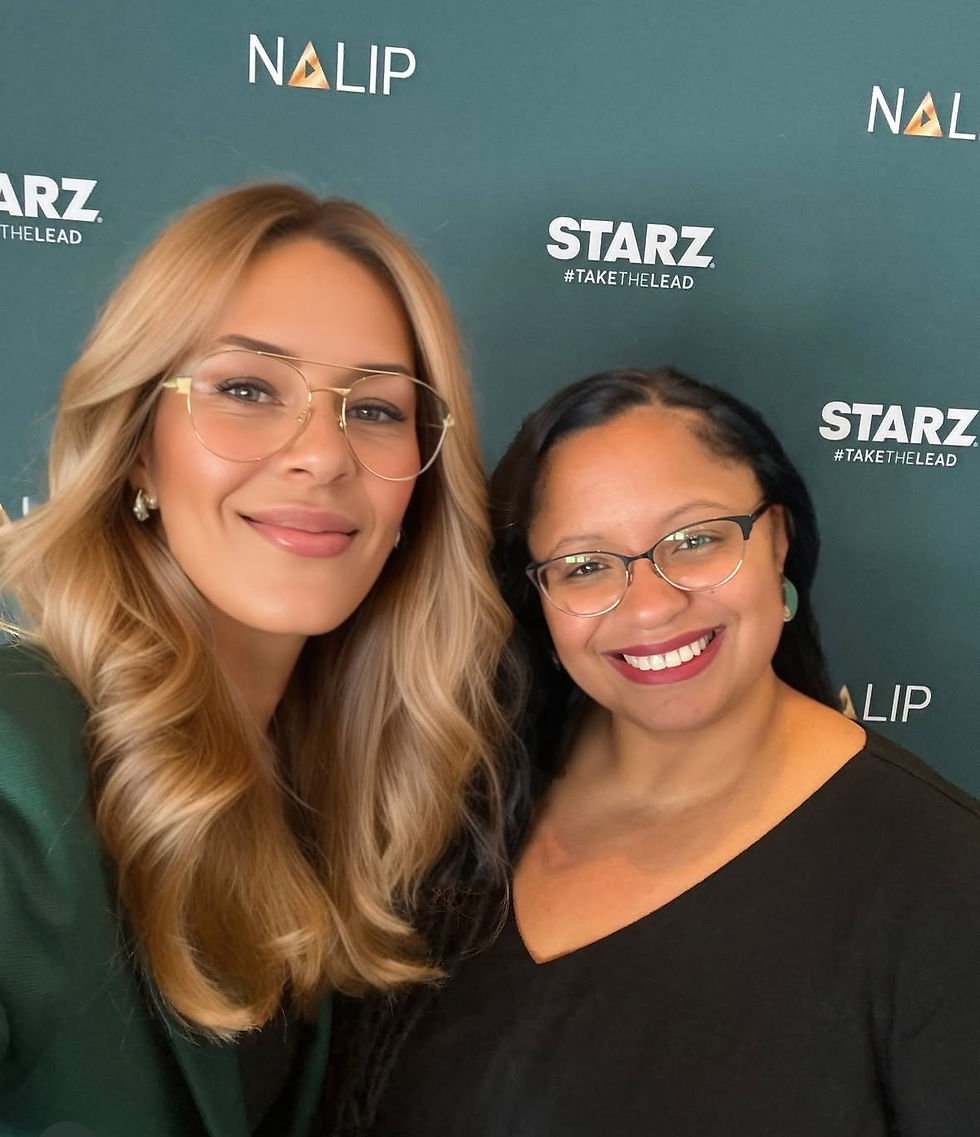 Two women smile at the camera: Jenna Cavelle, a woman with light brown skin and dark blond hair stands at the left, Eunice Levis, a slightly shorter woman with brown skin and dark hair stands on the right. 