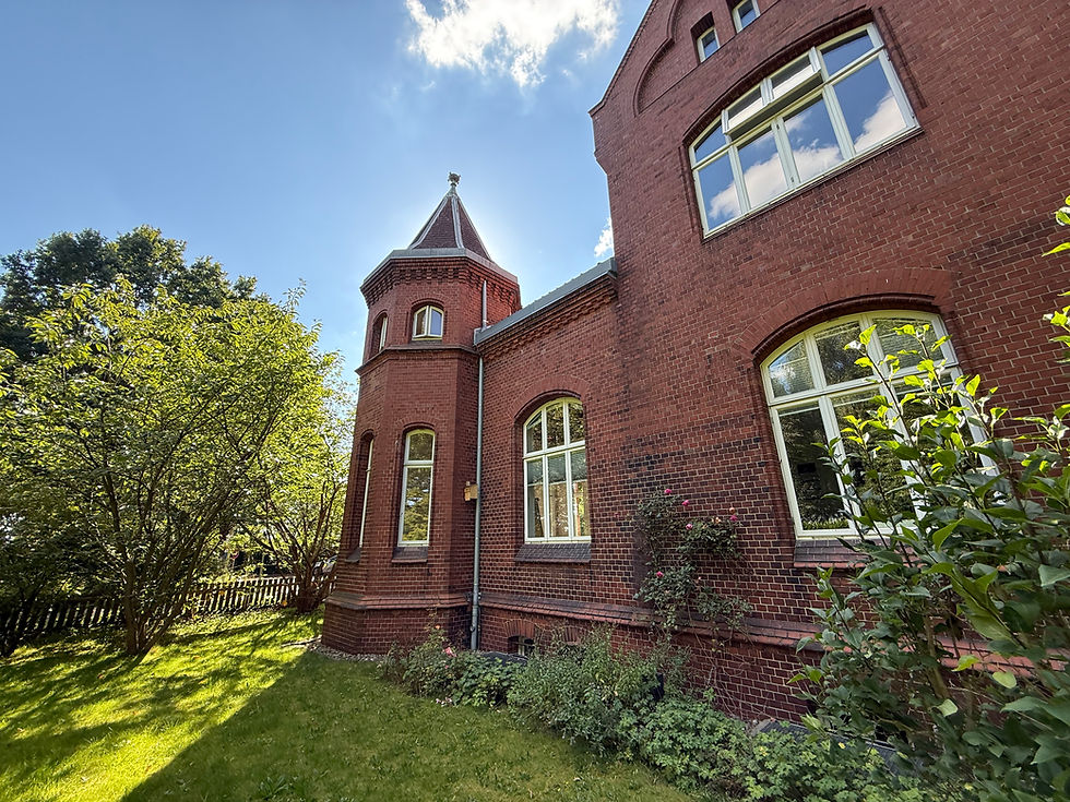 Photo of our office building with a blue sky and green trees. It is an old pilot's house in Kiel Holtenau, built of red brick.
