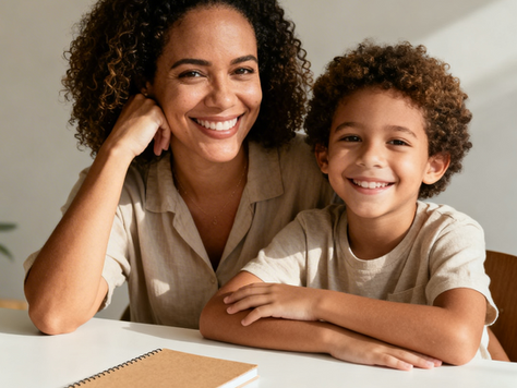 Mulher e criança brasileiras sentadas à mesa em um momento de estudo leve e afetuoso. Elas trocam olhares de cumplicidade e sorrisos em um ambiente doméstico acolhedor com iluminação natural.