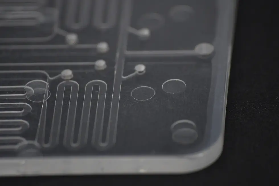 Close-up of precision microfluidic chip showing molded microchannel geometry and optical-grade PMMA surface quality