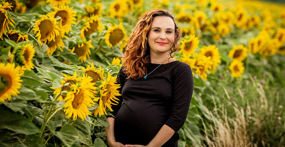 Pregnant woman in a black dress stands in front of sunflowers, Těhotenské .