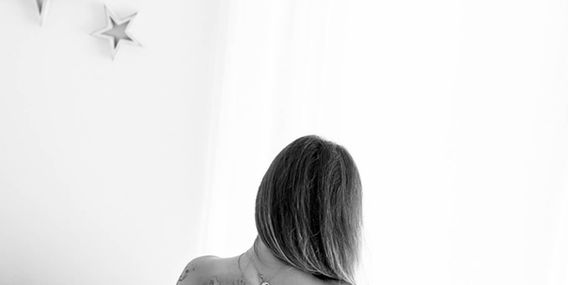 Žena s tetováním na zádech sedí na posteli, Boudoir a akty ženy.