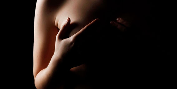 Žena zakrývá prsa rukou, boudoir a akty ženy, tmavé pozadí, intimní portrét.