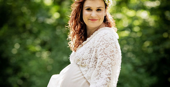 Žena v bílých šatech, s květinovým věncem, těhotenské na pozadí lesa.