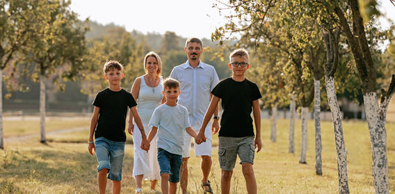 Usísměv rodina chodí spolu držíci se za ruce v parku Rodinné zelené stromy