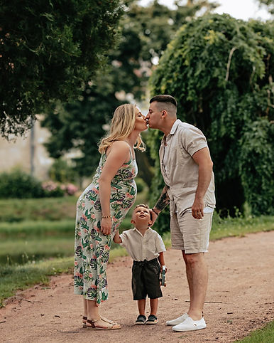 Kissing couple with child holding hands, Těhotenské, family photo in park setting.