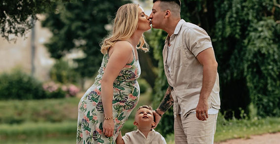 Man and woman kissing with child, happy family in a park. Těhotenské .