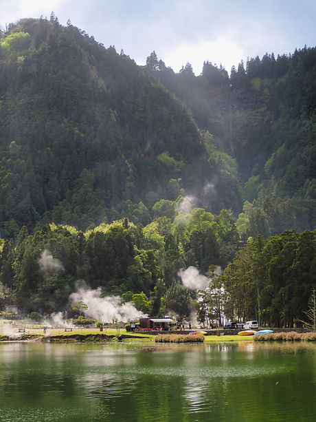Fumaroles at Lake Furnas, seen from across the lake. There are high tree-covered hillsides in the background