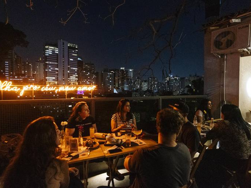 Movimento noturno em mesas de bar em uma calçada urbana.