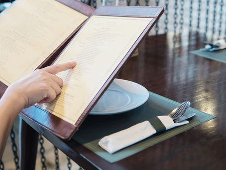 Imagem editorial minimalista. Um cardápio curto sobre mesa de madeira, tipografia clássica, poucas opções visíveis.