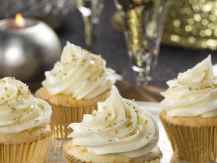 Cupcake com cobertura perolada e pó dourado refletindo sob luz suave.