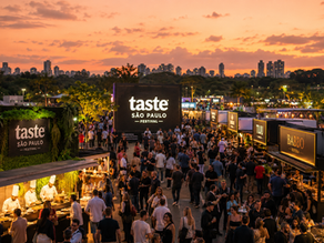 Imagem editorial ampla do Taste São Paulo Festival ao entardecer, com estandes gastronômicos iluminados, chefs em ação, público circulando entre experiências e o verde do Parque Villa-Lobos ao fundo